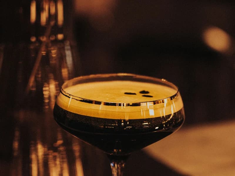 A coupe of espresso martini, its crema and coffee beans lit on a dark bar