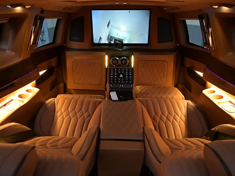 The rear cabin of a luxury van: quilted tan leather seats, warm lighting and a screen