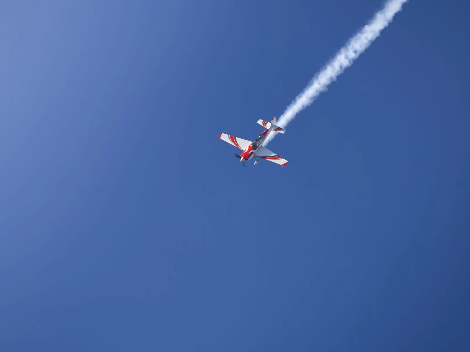 A red and white aerobatic aeroplane trailing smoke against a deep blue sky