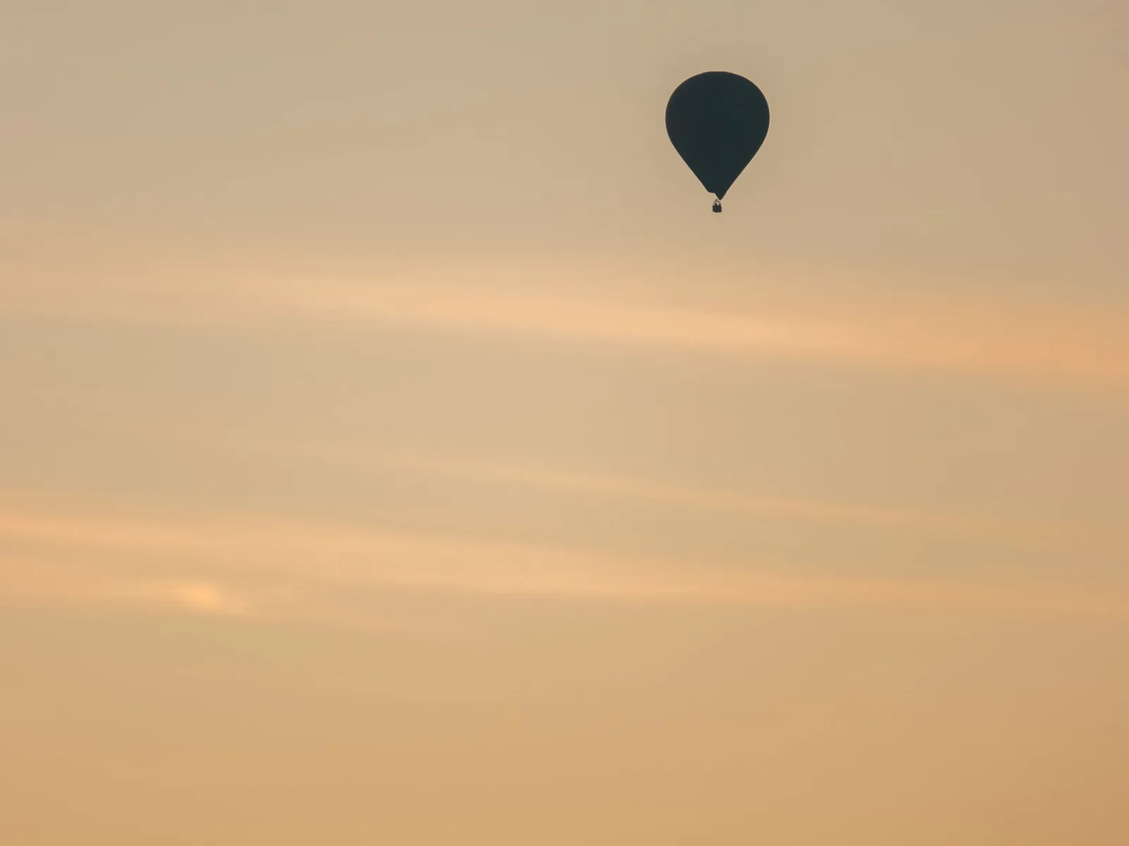 A hot air balloon in silhouette high in a pale gold sky at sunrise
