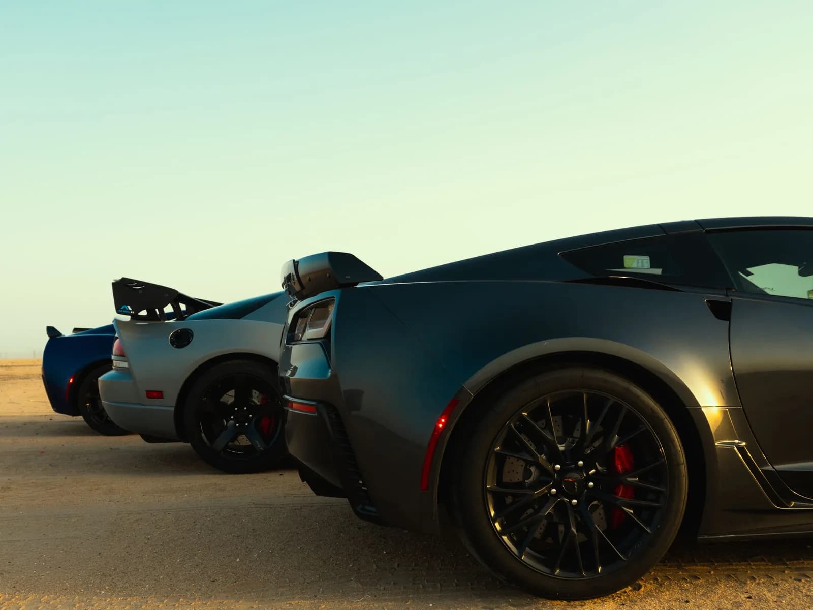 Three supercars parked nose to tail on desert sand at the end of the day
