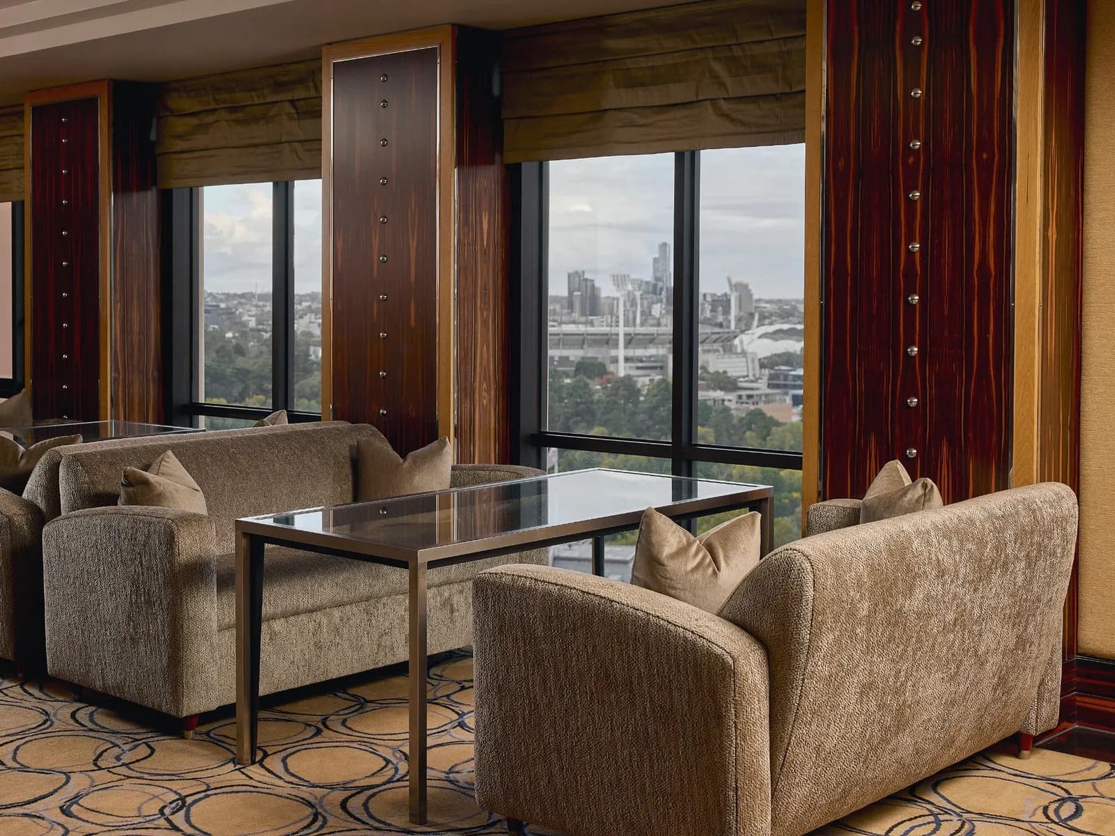 A private lounge of low armchairs behind full-height glass, the city and its parkland outside