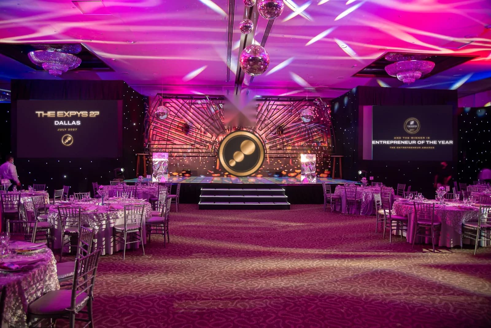 A violet-lit ballroom with a stage between two screens, THE EXPYS 27 and Dallas on the left