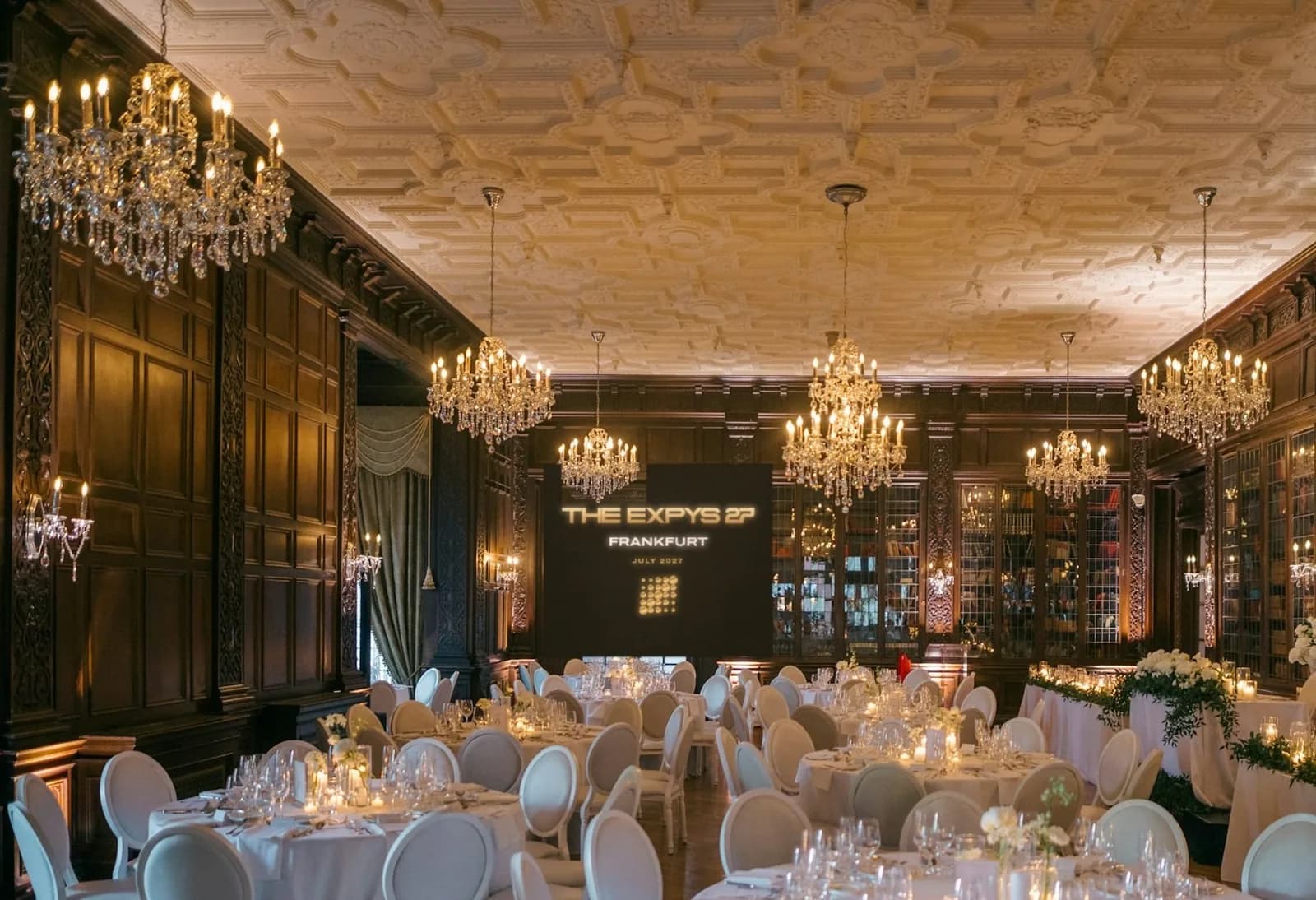 A panelled library ballroom under crystal chandeliers, white rounds of ten, THE EXPYS 27 and Frankfurt on the screen at the far end