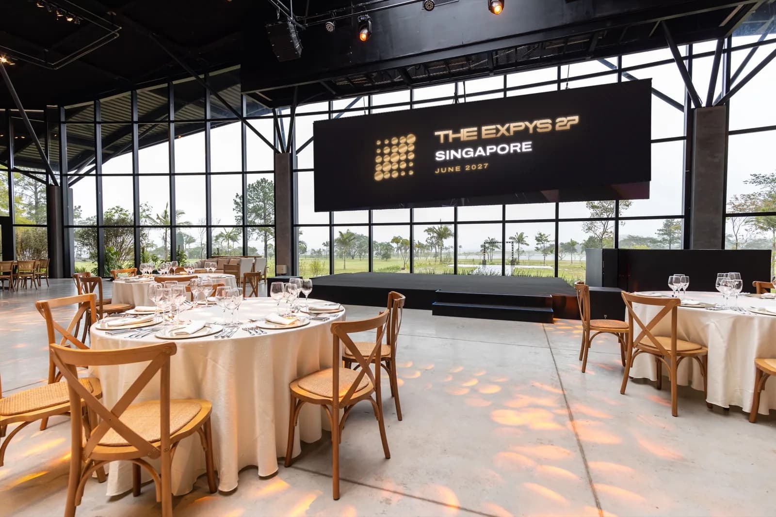 A glass-walled hall set for dinner, THE EXPYS 27 and Singapore on the screen over the stage