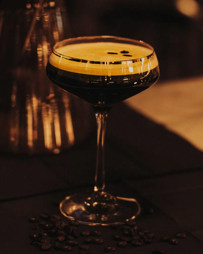 A coupe of espresso martini with coffee beans on a dark bar