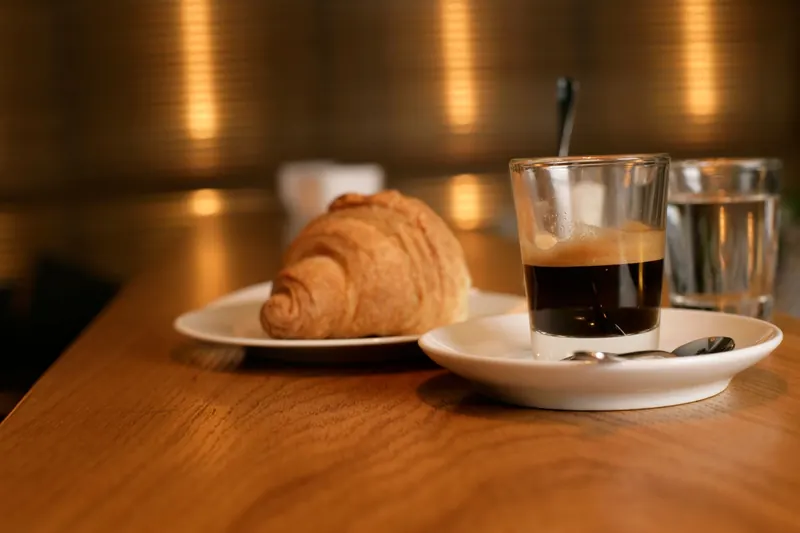 A croissant and an espresso on a warm wooden table