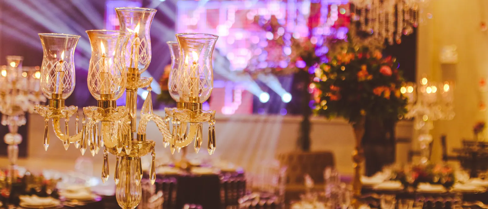 A ballroom set for a gala dinner, crystal candelabras lit on the tables and stage lights beyond