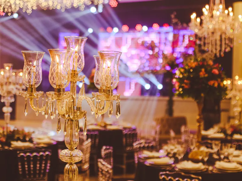 A ballroom set for a gala dinner, crystal candelabras lit on the tables and stage lights beyond