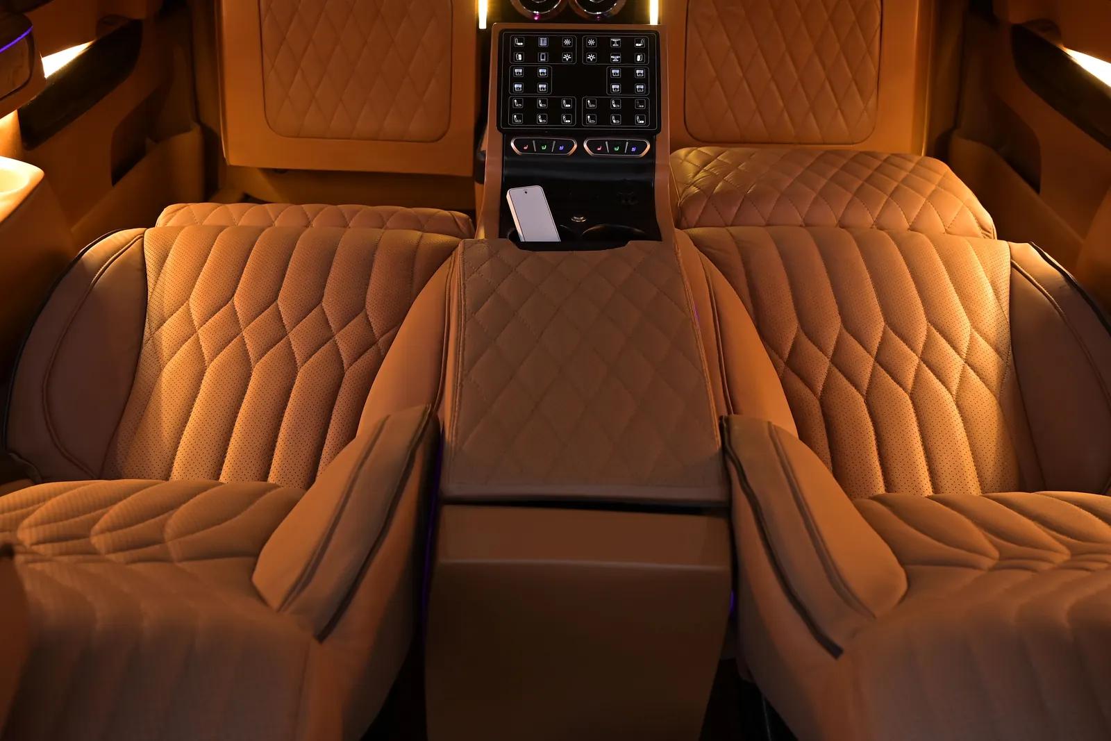 Quilted leather lounge seats in the back of a chauffeured van, warmly lit